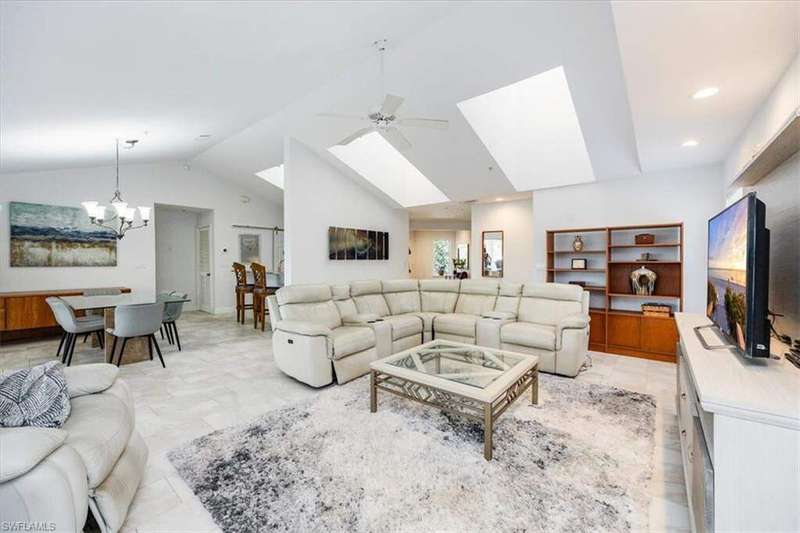 Living room with ceiling fan with notable chandelier, high vaulted ceiling, and a skylight