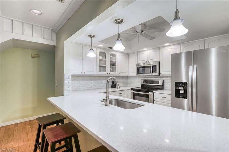 Kitchen featuring stainless steel appliances, hanging light fixtures, a kitchen breakfast bar, glass insert cabinets, and tasteful backsplash