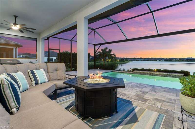 View of patio / terrace featuring a sunroom, a lanai, an outdoor living space with a fire pit, a water view, and an outdoor pool