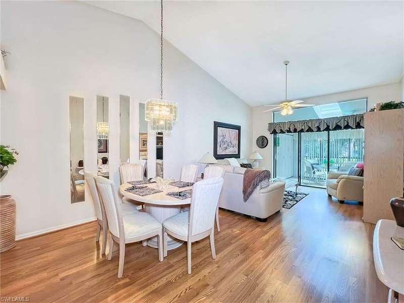 Dining room with ceiling fan with notable chandelier, light wood-type flooring, and high vaulted ceiling