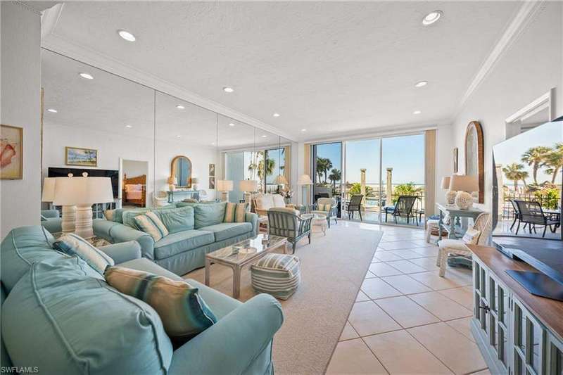 Tiled living room featuring crown molding, volume ceilings, expansive mirrored wall, view of the porch/lanai, pool and the Gulf of Mexico beyond...