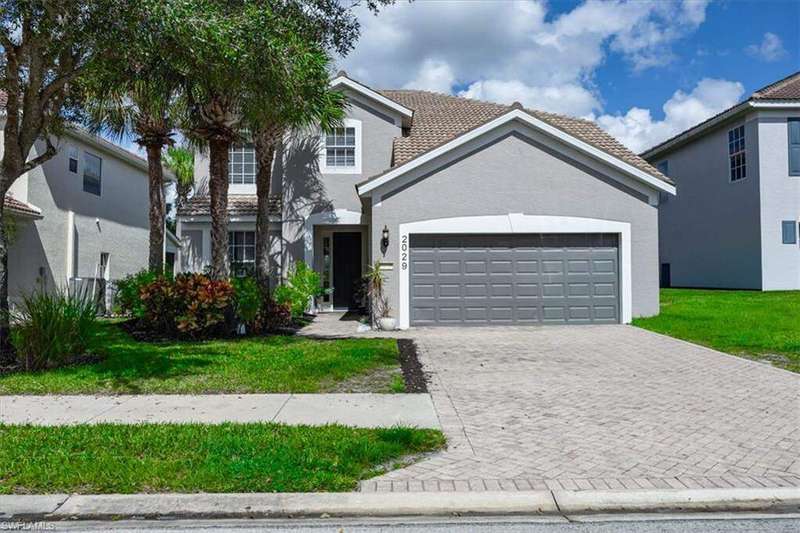 Traditional home featuring decorative driveway, an attached garage, stucco siding, and a front lawn