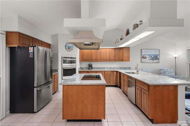 Kitchen with appliances with stainless steel finishes, a peninsula, a kitchen island, brown cabinets, and light stone counters