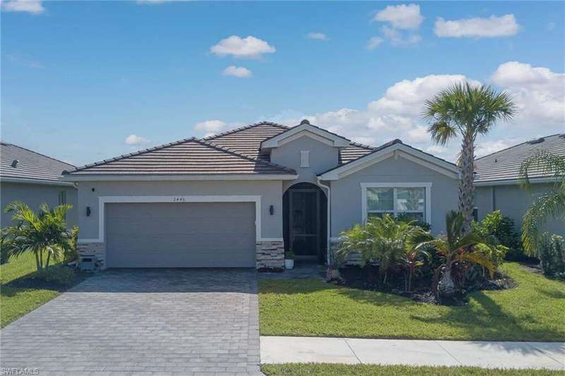 View of front of house with stucco siding, stone siding, an attached garage, a front lawn, and decorative driveway