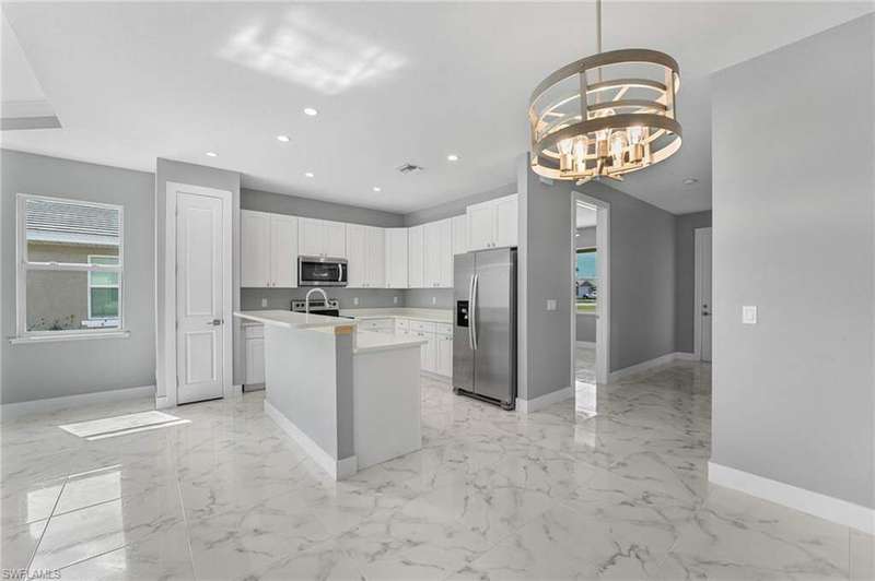 Kitchen featuring white cabinets, a chandelier, an island with sink, pendant lighting, and appliances with stainless steel finishes