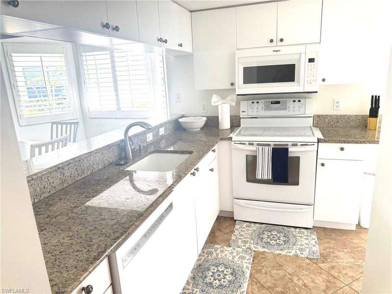 Kitchen featuring white appliances, a peninsula, white cabinetry, dark stone countertops, and a sink