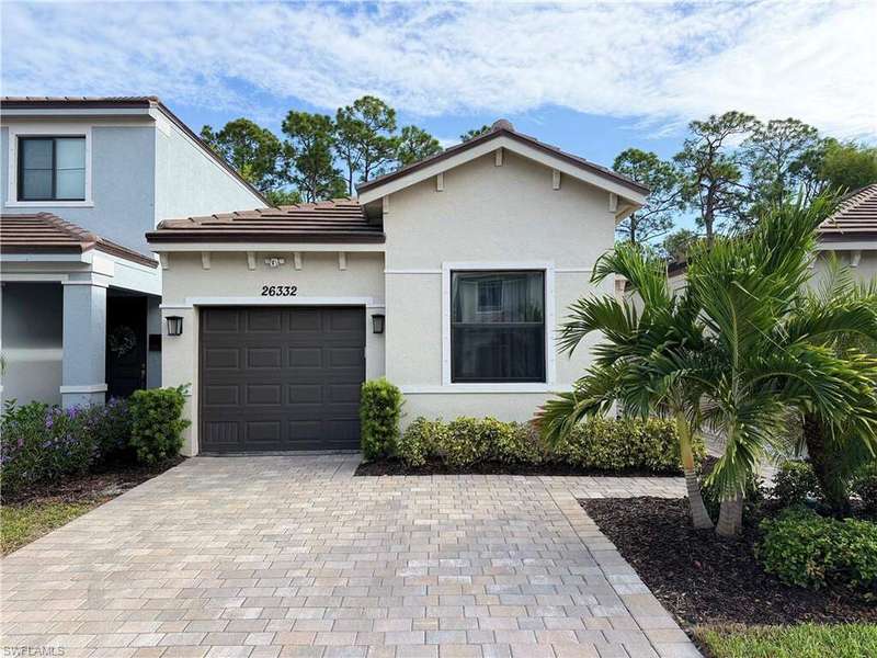 View of front facade featuring a tiled roof, decorative driveway, stucco siding, and a garage