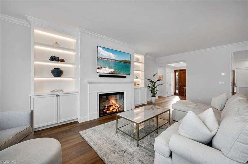 Living room with built in shelves, crown molding, a glass covered fireplace, and dark wood-style floors