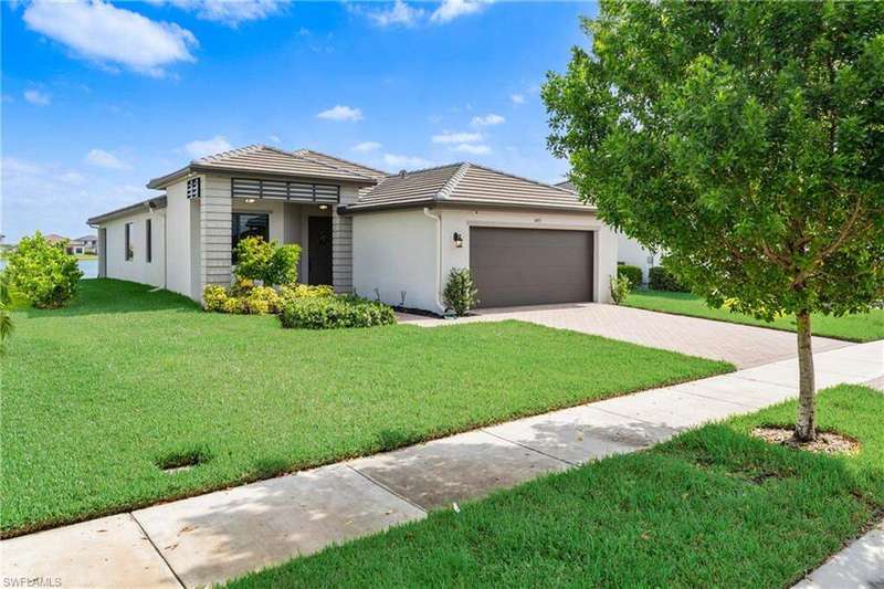 View of front of house with an attached garage, driveway, a tiled roof, and a front lawn