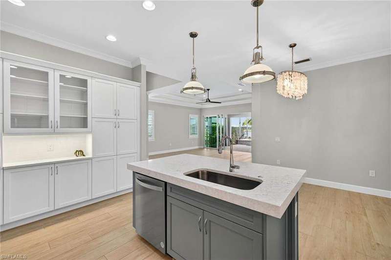 Kitchen with light wood-style floors, gray cabinets, crown molding, white cabinetry, and glass insert cabinets