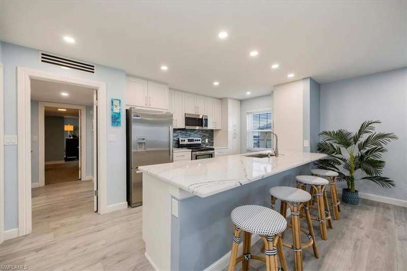 Kitchen with white cabinets, light stone counters, appliances with stainless steel finishes, a breakfast bar, and light wood finished floors