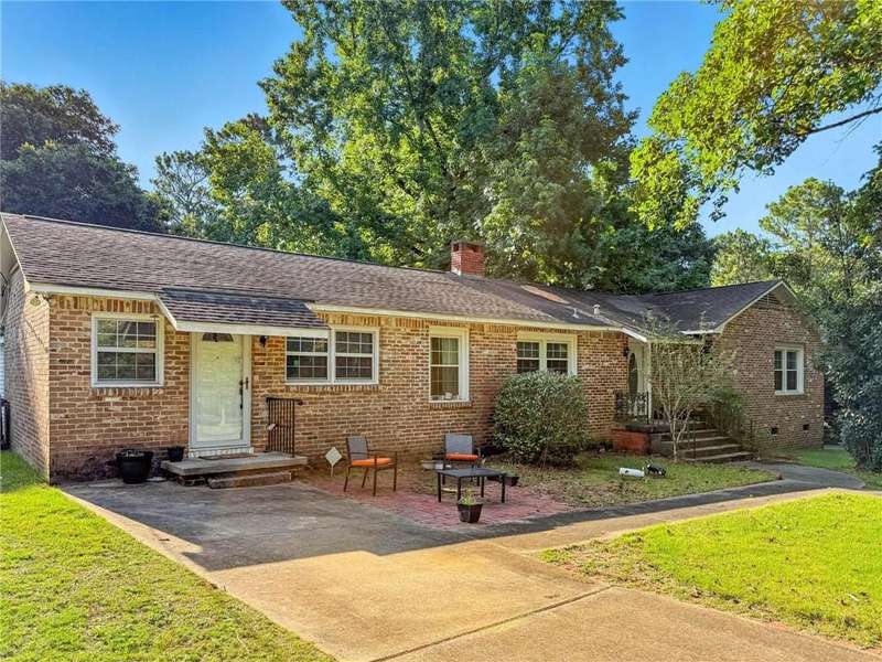 View of front facade with brick siding, a front yard, a chimney, and a shingled roof