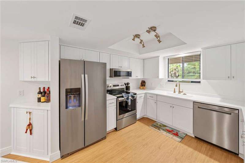 Kitchen featuring stainless steel appliances, white cabinets, light wood-style flooring, and a tray ceiling