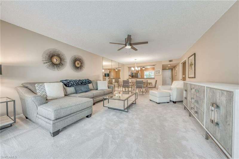 Carpeted living room featuring ceiling fan with notable chandelier and a textured ceiling