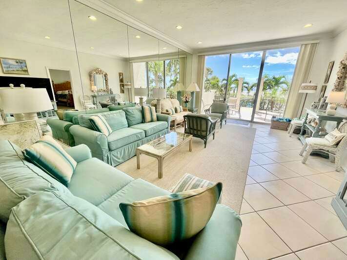 Tiled living room featuring crown molding, volume ceilings, expansive mirrored wall, view of the porch/lanai, pool and the Gulf of Mexico beyond...