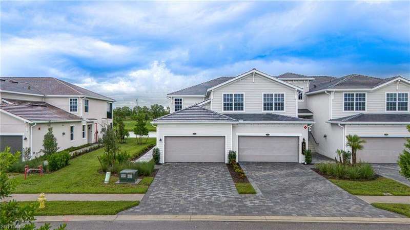 Traditional home with decorative driveway, a tiled roof, an attached garage, a front lawn, and a residential view