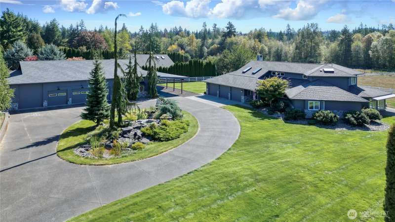 Drone view of front of property, custom 3500+ sq ft home on right, 3000 sq ft shop on left with attached carport. I love the paved circle drive, the massive water feature and Koi in the middle and the Dr. Seuss trees!
