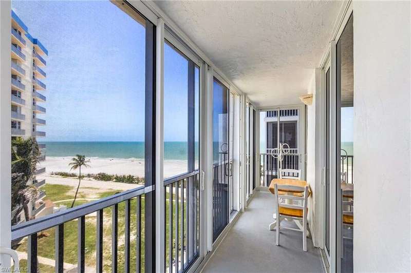 Sunroom / solarium with view of water and beach, a wall of windows, a textured ceiling, and carpet flooring