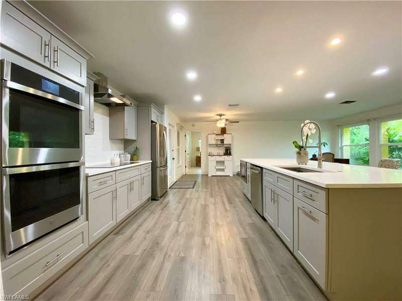 Kitchen with gray cabinets, stainless steel appliances, light wood-type flooring, and an island with sink