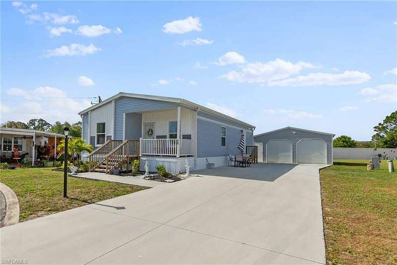 Manufactured / mobile home featuring covered porch, a front lawn, an outbuilding, and a garage