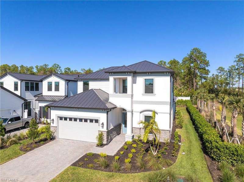 View of front of home with a standing seam roof, a metal roof, an attached garage, driveway, and stone siding