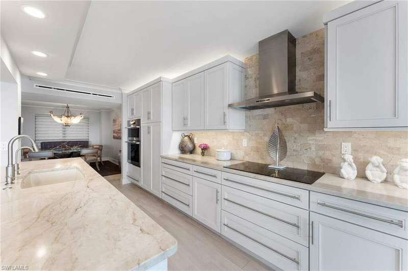 Kitchen with sink, wall chimney exhaust hood, light stone countertops, tasteful backsplash, and light hardwood / wood-style floors