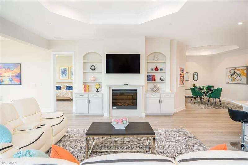 Living area featuring a raised ceiling, built in features, light wood-style flooring, a glass covered fireplace, and recessed lighting