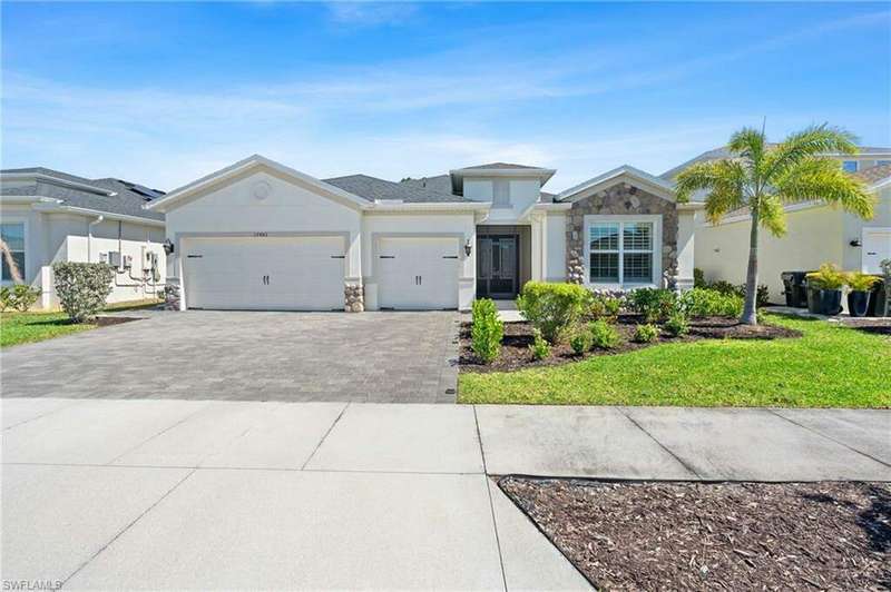 View of front of home with an attached garage, stone siding, decorative driveway, and stucco siding