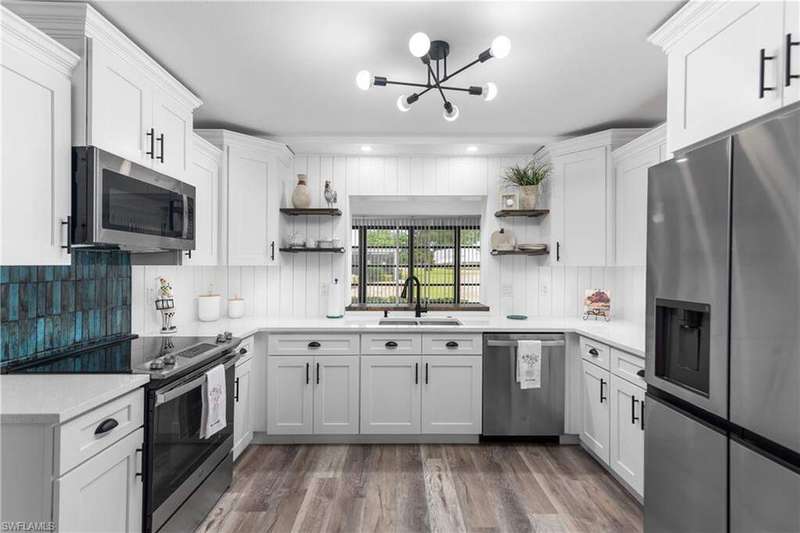Kitchen featuring stainless steel appliances, open shelves, a chandelier, dark wood-style flooring, and light stone counters