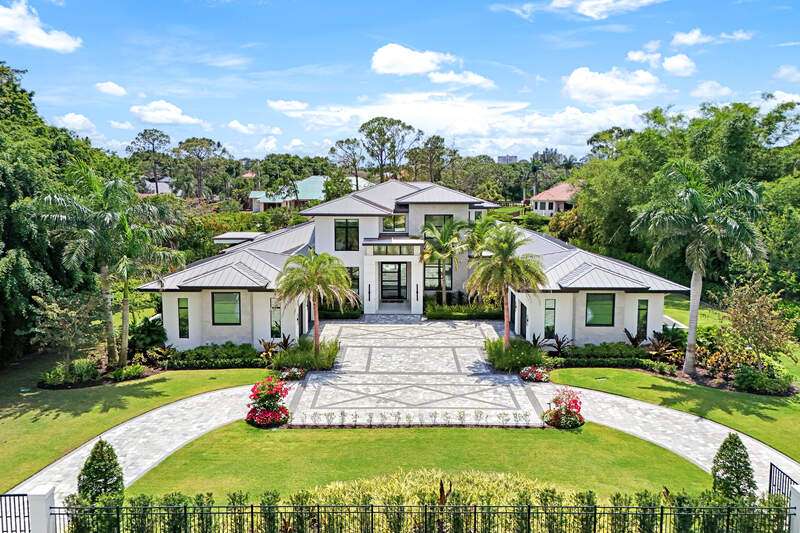View of front facade with curved driveway, stucco siding, and a standing seam roof