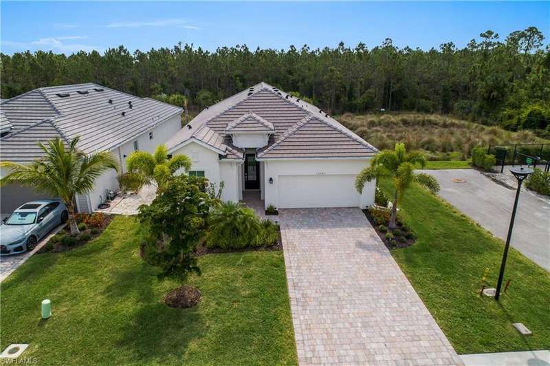Single story home with a wooded view, an attached garage, decorative driveway, stucco siding, and a front yard