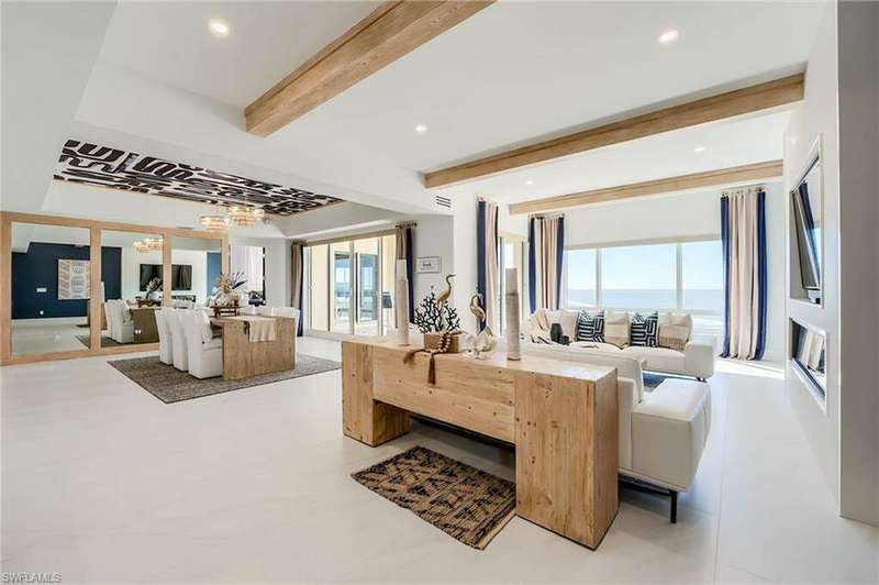 Living room and dining room featuring dramatic wood beams and wallpaper.  Mirrored wall in dining makes space seem larger