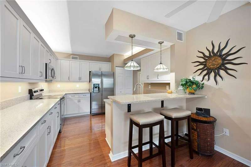 Kitchen with granite counters, hardwood  floors, stainless steel appliances, white wood shaker style cabinets, and breakfast bar