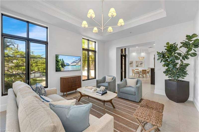 Living room with crown molding, a notable chandelier, light tile patterned floors, and a raised ceiling