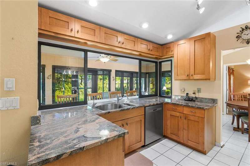 Kitchen featuring ceiling fan, dark stone countertops, stainless steel dishwasher, light tile patterned floors, and brown cabinetry