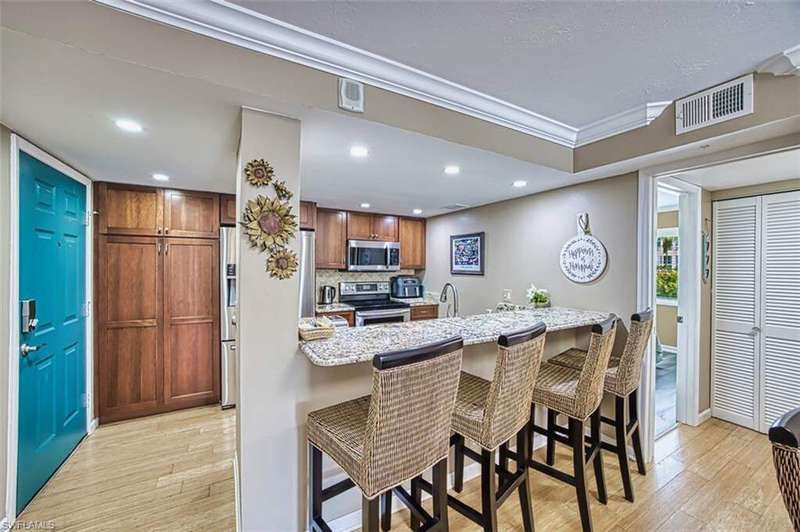 Kitchen with appliances with stainless steel finishes, light wood-style floors, a kitchen breakfast bar, recessed lighting, and light stone countertops