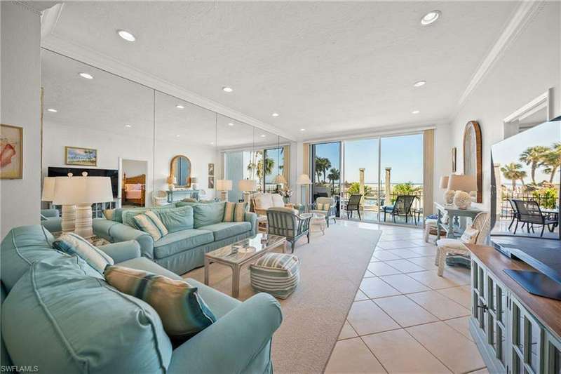 Tiled living room featuring crown molding, volume ceilings, expansive mirrored wall, view of the porch/lanai, pool and the Gulf of Mexico beyond...