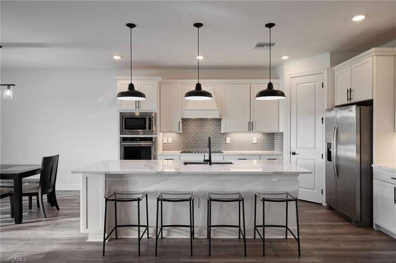 Kitchen with white cabinetry, chef's kitchen, stainless steel appliances, kitchen island with sink, and decorative light fixtures