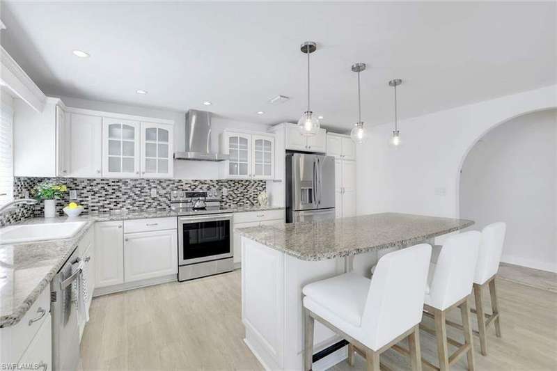 Kitchen featuring a large kitchen island, granite countertops, wall chimney exhaust hood, appliances with stainless steel finishes, and decorative light fixtures.