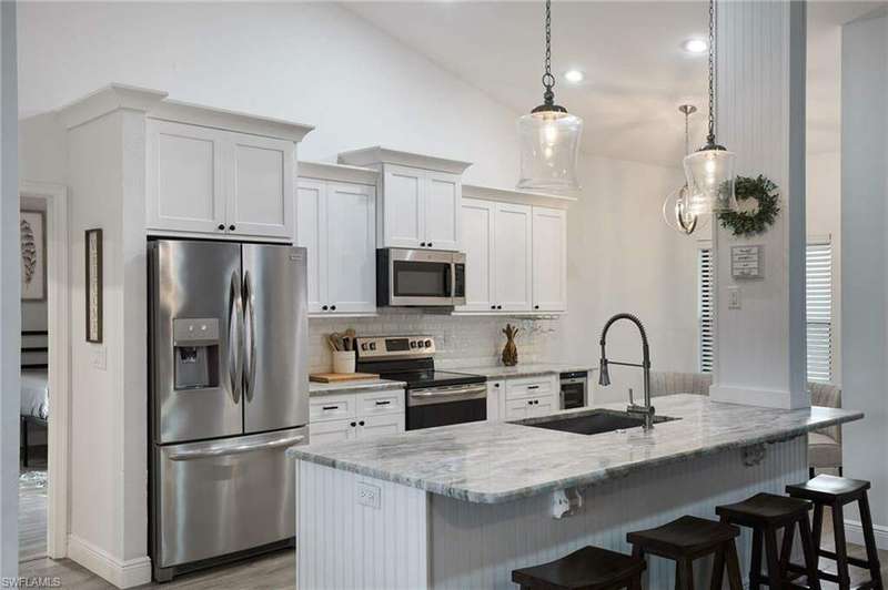 Kitchen featuring an island with sink, light stone counters, white cabinets, hanging light fixtures, and appliances with stainless steel finishes